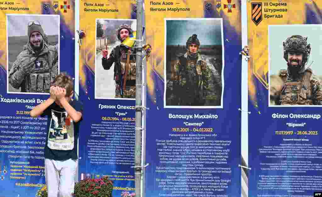 A boy reacts near placards depicting dead Ukrainian servicemen of the Azov Brigade at an open air exhibition in Kyiv, amid Russian invasion in Ukraine.