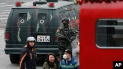 People walk past an armed Chinese paramilitary policeman standing guard in the capital city's popular shopping and nightlife area of Sanlitun in Beijing, Dec. 27, 2015.