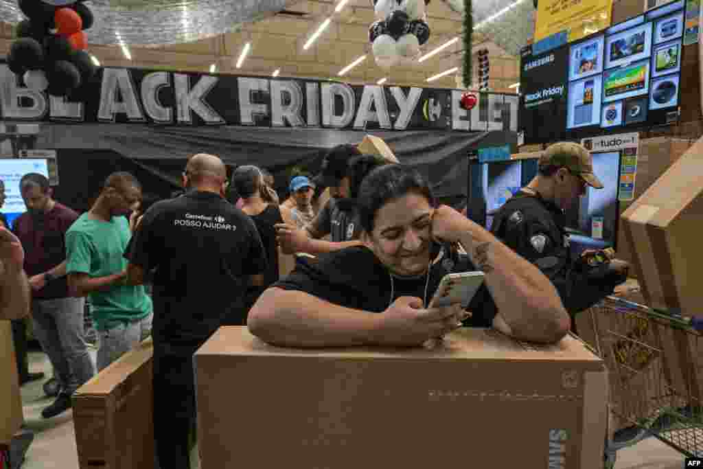 A woman watches her phone while shoppers buy TV sets at a supermarket during a Black Friday sale in Sao Paulo on Nov. 28, 2024.