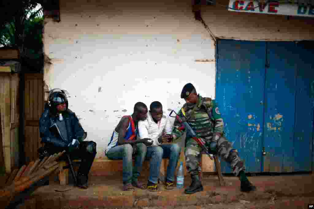 A uniformed FOMAC peacekeeper chats with local boys while another one dressed in full riot gear sits in the tense combatant neighborhood of Bangui, Central African Republic, Dec. 16, 2013.