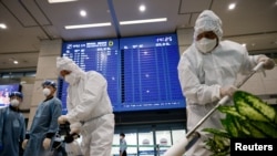 Des travailleurs portant un équipement de protection désinfectent une porte d'arrivée car une carte électronique affiche les informations d'arrivée au milieu de la pandémie de coronavirus à l'aéroport international d'Incheon à Incheon, en Corée du Sud, le 28 décembre 2020.