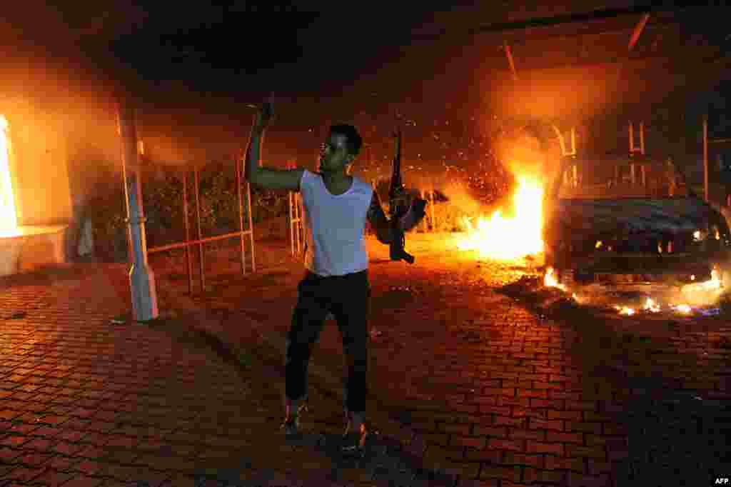 An armed man waves his rifle as buildings and cars are engulfed in flames after being set on fire inside the U.S. consulate compound in Benghazi, Libya, late on September 11, 2012.
