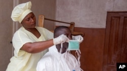 Healthcare worker helps colleague prepare protective equipment before entering Ebola isolation ward, Kenema Government Hospital, Kenema, Sierra Leone, Aug. 12, 2014.