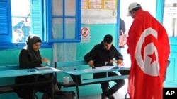 FILE - A Tunisian draped in the national flag arrives at a polling station to vote in La Marsa, outskirts of Tunis, Tunisia, Dec, 21, 2014.