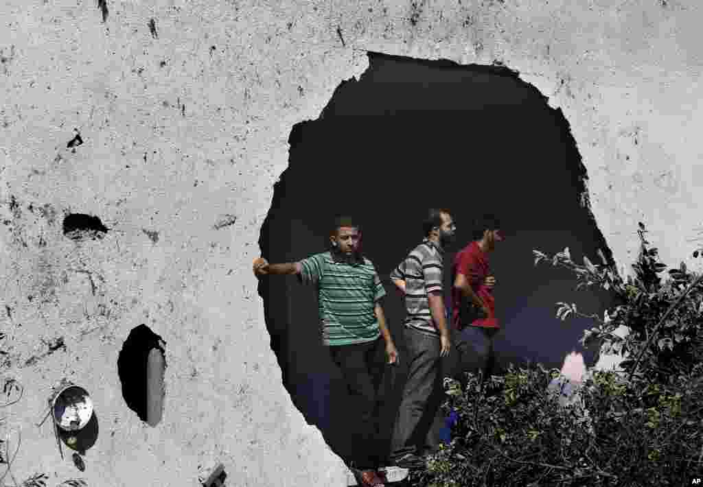 Palestinians standing next to a damaged wall watch rescuers searching for bodies and survivors under the rubble of an apartment building that was destroyed by an Israeli missile strike, in Gaza City, July 21, 2014.