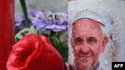 Sebuah lilin yang menggambarkan Paus Fransiskus diletakkan di patung Yohanes Paulus II di luar rumah sakit Gemelli tempat Paus Fransiskus dirawat di Roma, Selasa, 25 Februari 2025. (Foto: Tiziana Fabi/AFP)