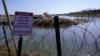 ARCHIVO - Migrantes cruzan el Río Grande hacia EEUU desde México detrás de un alambre de púas y un letrero que advierte que es peligroso e ilegal cruzar, el 3 de enero de 2024, en Eagle Pass, Texas.