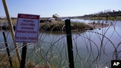 ARCHIVO - Migrantes cruzan el Río Grande hacia EEUU desde México detrás de un alambre de púas y un letrero que advierte que es peligroso e ilegal cruzar, el 3 de enero de 2024, en Eagle Pass, Texas.
