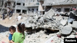 A Palestinian girl carries a boy amid the rubble of their houses which were destroyed by Israeli air strikes during the Israel-Hamas fighting in Gaza, May 23, 2021. 