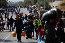 FILE - Migrants carry their belongings as they flee a road leading from Moria to the capital of Mytilene, on the northeastern island of Lesbos, Greece, Sept. 17, 2020.