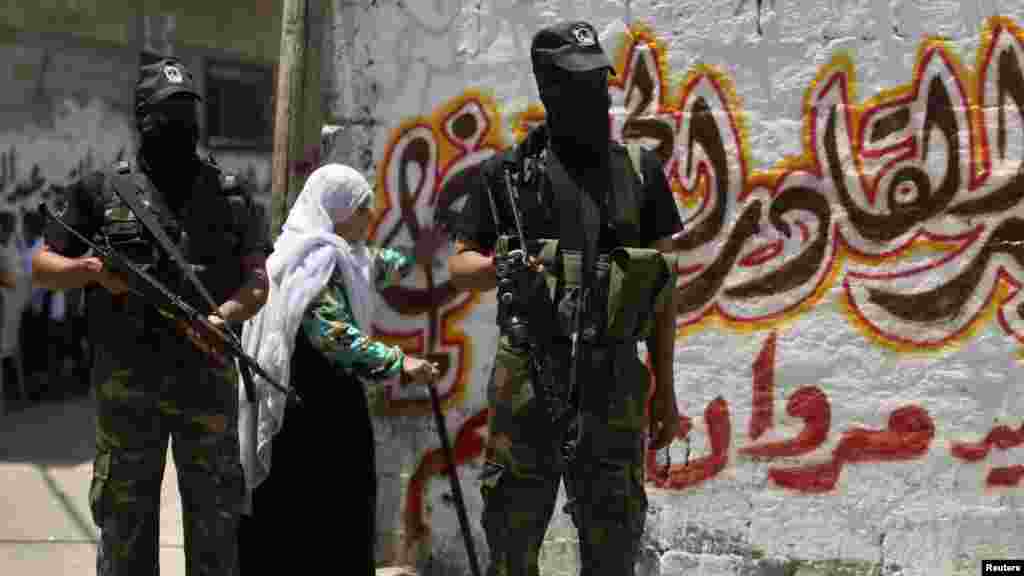 A woman walks behind Palestinian militants standing guard during the funeral of their comrade Marwan Sleem in the central Gaza Strip, July 7, 2014.