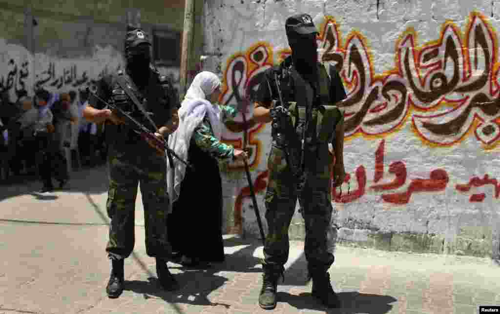 Seorang perempuan berjalan di belakang para militan Palestina yang menjaga upacara pemakaman kawan mereka Marwan Sleem di Jalur Gaza bagian tengah (7/7).