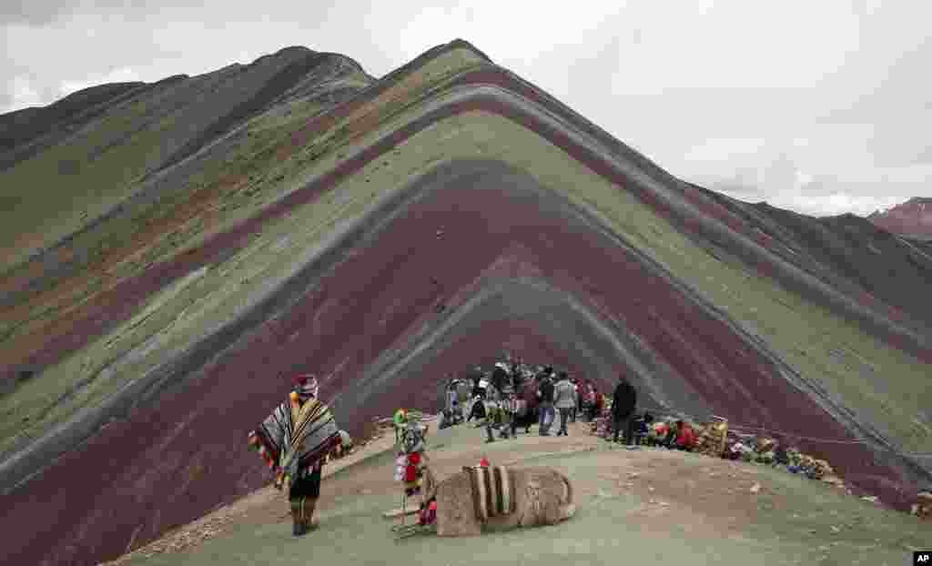 បុរសជនជាតិ Andean ឈប់សម្រាកជាមួយសត្វ llama របស់ខ្លួននៅពេលដែលភ្ញៀវទេសចរទស្សនាភ្នំឥន្ធនូធម្មជាតិនៅទីក្រុង Pitumarca ប្រទេសប៉េរូ។