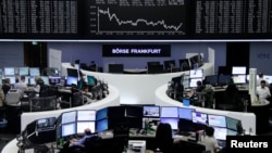 FILE - Traders work at their desks in front of the German share price index, DAX board, at the stock exchange in Frankfurt, Germany, Feb. 16, 2016.