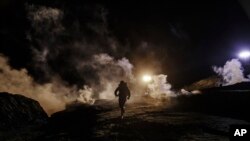 Para migran lari menghindari tembakan gas air mata dari para petugas perlindungan perbatasan di pagar pembatas sisi wilayah Meksiko setelah mereka memanjat pagar untuk menyeberang ke San Diego, dari Tijuana, Meksiko, 1 Januari 2018. 