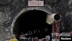 Members of rescue teams stand at the entrance of a tunnel where road workers are trapped after a portion of the tunnel collapsed in Uttarkashi