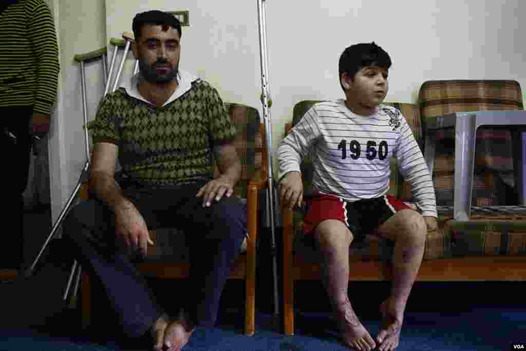 A wounded Syrian rebel sits beside a boy in Amman, Jordan. The boy was hurt in a missile strike on his home in Dara, Syria. (Y. Weeks/VOA)