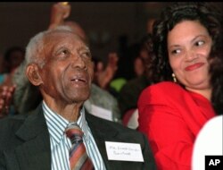 FILE - Tuskegee syphilis study survivor Ernest Hendon, 90, smiles while watching then-President Bill Clinton give a public apology, via video telecast, at the Kellogg Executive Conference Center in Tuskegee, Alabama, May 16, 1997. At right is Ethel Talley of the Macon County Health Department.
