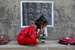 Seorang gadis, yang tidak memiliki akses ke fasilitas internet dan gadget, menggunakan mikroskop saat menghadiri kelas terbuka di luar rumah dengan dindingnya diubah menjadi papan tulis, pasca penutupan sekolah akibat pembatasan terkait COVID-19 di desa Joba Attpara, distrik Paschim Bardhaman, Bengala Barat, India (foto: Reuters).