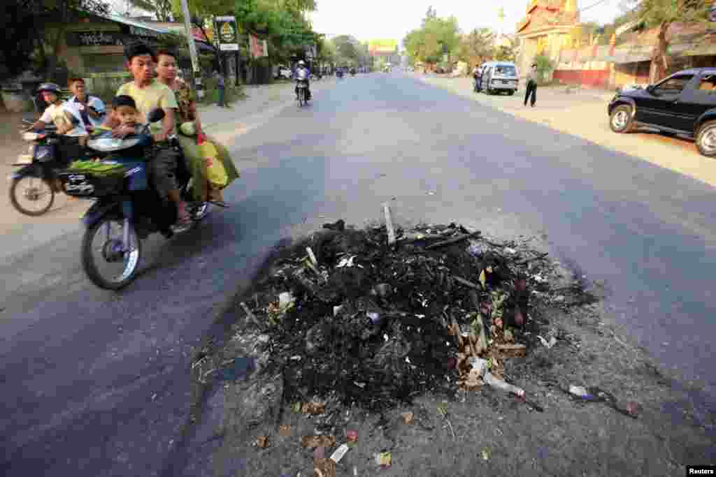 People ride their mopeds past the remains of two persons killed in clashes in Meikhtila March 22, 2013. 