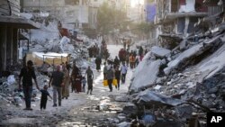 Warga Palestina yang mengungsi akibat serangan udara dan darat Israel di Jalur Gaza, berjalan melalui aliran limbah yang mengalir ke jalan-jalan kota selatan Khan Younis, Jalur Gaza, 4 Juli 2024. (Foto: AP)