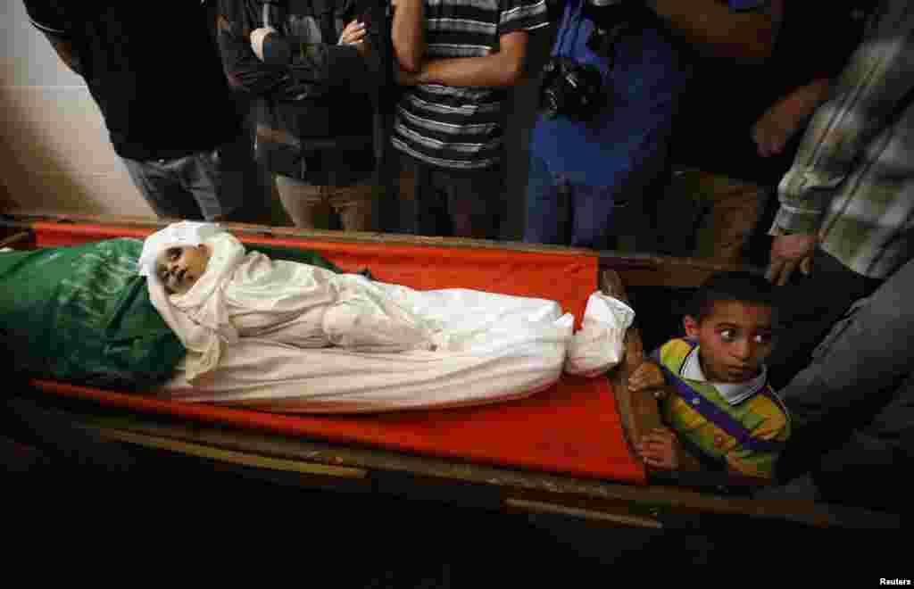 A Palestinian boy stands next to the bodies of the wife of Hamas's military leader, Mohammed Deif, and his infant son Ali, whom medics said were killed in Israeli air strikes, during their funeral, in the northern Gaza Strip, Aug. 20, 2014.