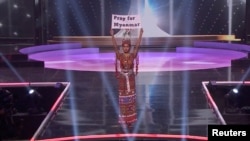 កញ្ញា Ma Thuzar Wint Lwin ដែល​ជា​បេក្ខជន​ Miss Universe តំណាង​ប្រទេស​មីយ៉ាន់ម៉ា លើក​បដា​មួយ​សរសេរ​ថា «បួងសួង​ឲ្យ​មីយ៉ាន់ម៉ា» ក្នុង​ពេល​ប្រឡង​វគ្គ​ផ្ដាច់ព្រ័ត្រ​នៅ​ទីក្រុង Hollywood រដ្ឋ Florida សហរដ្ឋ​អាមេរិក ថ្ងៃទី១៣ ខែឧសភា ឆ្នាំ២០២១។