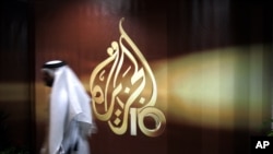 FILE - An employee of the Qatar-based Al-Jazeera network passes by an Al-Jazeera logo at the network's offices in Doha, Qatar.