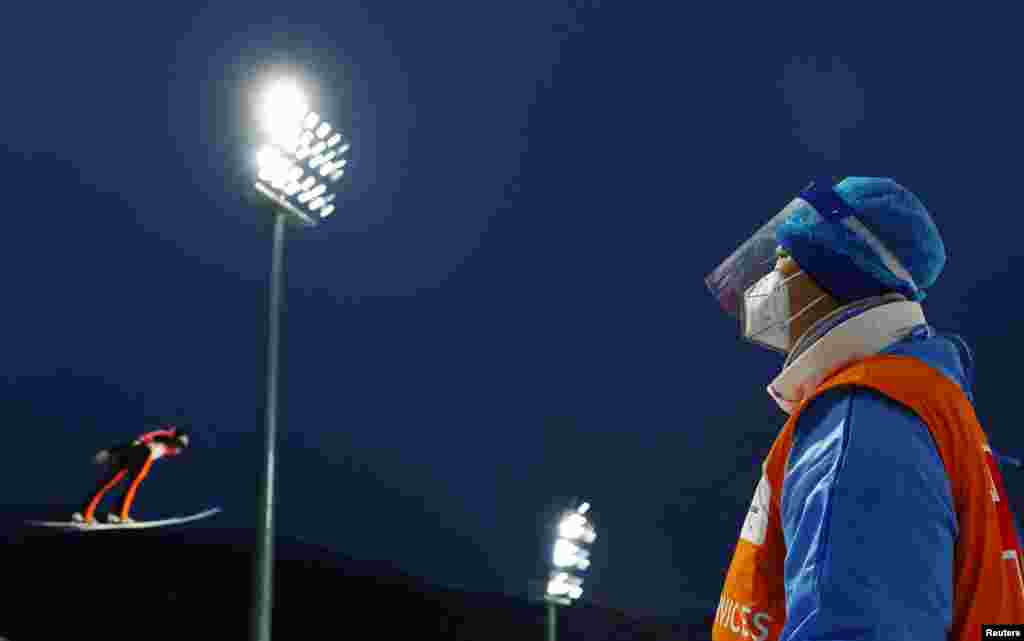 A member of the medical crew watches Andrei Feldorean of Romania in action during men's ski jumping at the 2022 Beijing Olympics, at the National Ski Jumping Centre, Zhangjiakou, China.