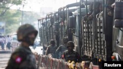 FILE - Soldiers stand next to military vehicles as people gather to protest the military coup in Yangon, Myanmar, on Feb. 15, 2021. Journalists working secretly in Myanmar say they "can be arrested by the military at any time," three years after the coup.