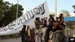 Pejuang Taliban berfoto sambil mengibarkan bendera di rumah gubernur Ghazni, di Ghazni, Afghanistan tenggara, 15 Agustus 2021. (Foto: AP)