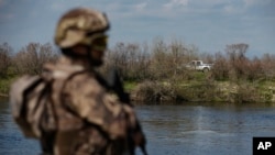 FILE - A Greek police vehicle, background, drives in front of a Turkish special forces team, front left, patrolling along the Maritsa river at the Turkish-Greek border near Karpuzlu village, in Edirne region, Turkey, March 11, 2020. 