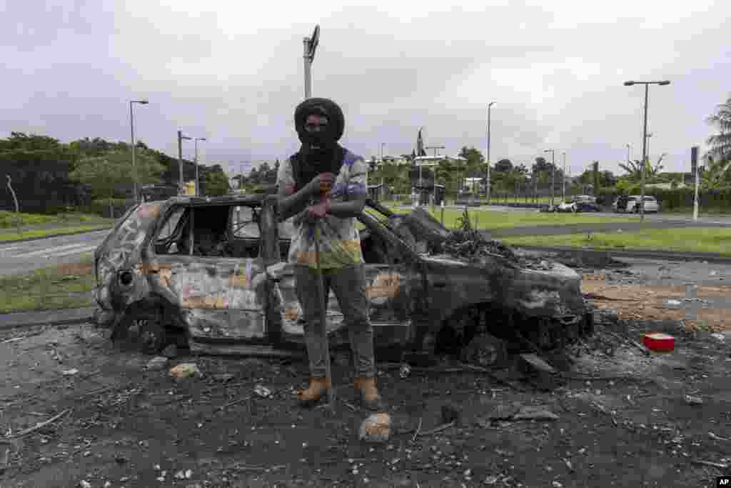 A man stands in front a burnt car after unrest in Noumea, New Caledonia, May 15, 2024. France has imposed a state of emergency in the Pacific territory for at least 12 days to boost security forces' powers to quell deadly unrest that has left four people dead, erupting after protests over voting reforms. 