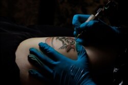 Tattoo artist Mike Chan's needle buzzes gently as he draws a design on his customer's thigh — a figure wearing a helmet, goggles and mask — in Hong Kong, Oct. 23, 2019.