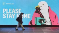 FILE - A woman walks past a sign urging people to stay home, in Melbourne, Australia, Aug. 14, 2020, as the city battles an outbreak of the coronavirus.