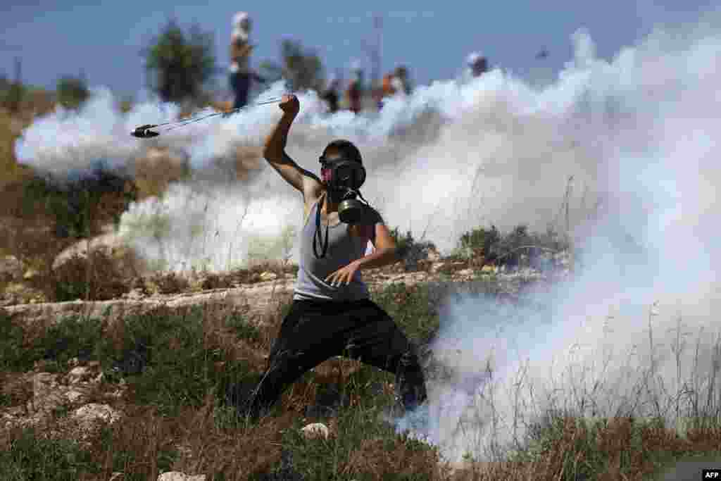 Seorang demonstran Palestina yang mengenakan masker, berusaha "mengembalikan" kaleng gas air mata yang ditembakkan oleh pasukan Israel pada aksi protes di desa Nabi Saleh, utara Ramallah, Tepi Barat yang diduduki Israel.