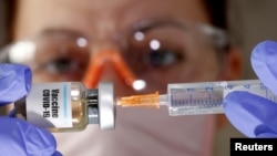 FILE - A woman holds a small bottle labeled with a "Vaccine COVID-19" sticker and a medical syringe in this illustration taken April 10, 2020.