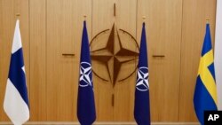 Bendera Finlandia (kiri) dan bendera Swedia (kanan) mengapit bendera NATO terpajang sebelum upacara penerimaan permohonan keanggotaan dari Finlandia dan Swedia, 18 Mei 2022. (Foto: Johanna Geron/Pool via AP)