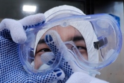 A worker cleans his goggles to spray disinfectant as a precaution against the coronavirus at a shopping district in Seoul, South Korea, Feb. 27, 2020.