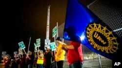 Jeff Elkins, de 37 años, empleado de una fábrica de GM, ondea una bandera del sindicato de trabajadores automotrices( United Auto Workers) al final del turno de medianoche de la Planta de Ensamblaje de Flint, Michigan. Sep.16 de 2019. Foto: Jake May/The Flint Journal via AP.