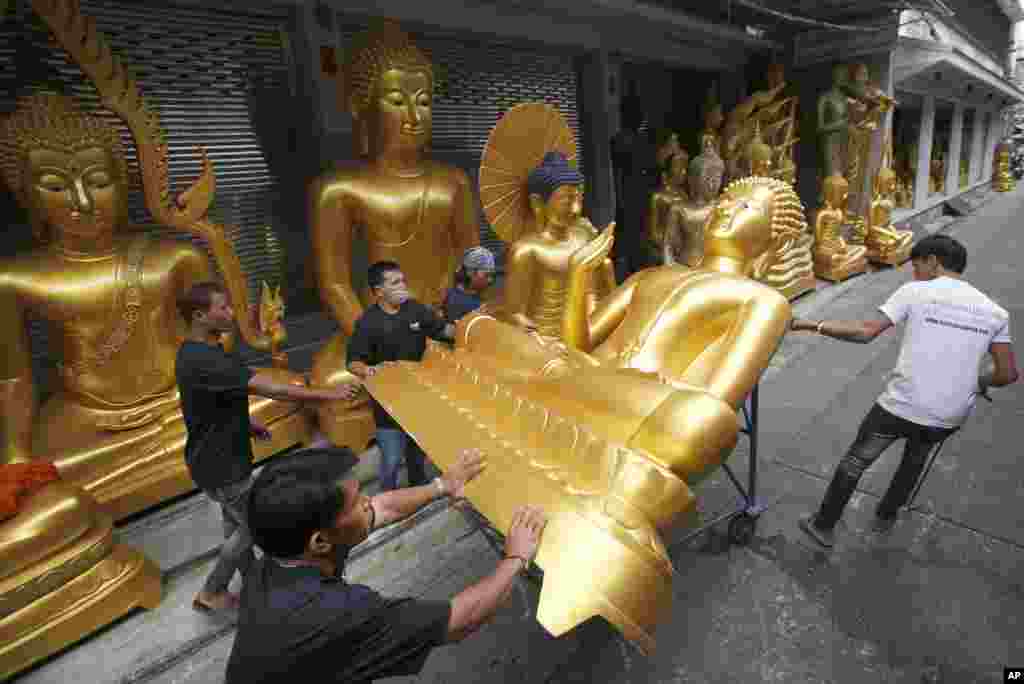 កម្មករកំពុងលើករូបសំណាកព្រះពុទ្ធនៅក្នុងហាងនៅទីក្រុងបាងកកប្រទេសថៃដើម្បីរៀបចំសម្រាប់ថ្ងៃចូលវស្សាខាងមុខ។