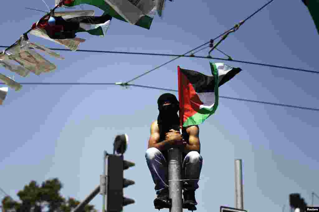 Seorang pemuda Palestina bertopeng duduk di atas tiang saat menyaksikan upacara pemakaman Mohammed Abu Khudair, 16, di Shuafat, pinggiran kota Arab di Yerusalem (4/7). (Reuters/Finbarr O'Reilly)