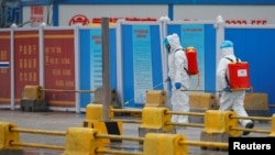 Pekerja dengan menggunakan APD menyemprot tanah dengan diinfektan di Pasar Baishazhou selama kunjungan tim Organisasi Kesehatan Dunia (WHO) untuk menyelidiki asal-usul pandemi virus corona, di Wuhan, Hubei, China. (Foto: Reuters)
