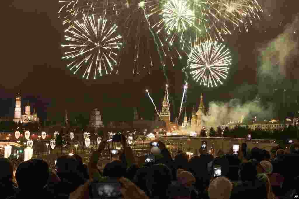 2018年1月1日,在俄罗斯莫斯科举行的新年庆祝活动中,烟花爆竹在克里姆林宫上空怒放,人们仰望和拍照。新年是俄罗斯的主要馈赠节日。