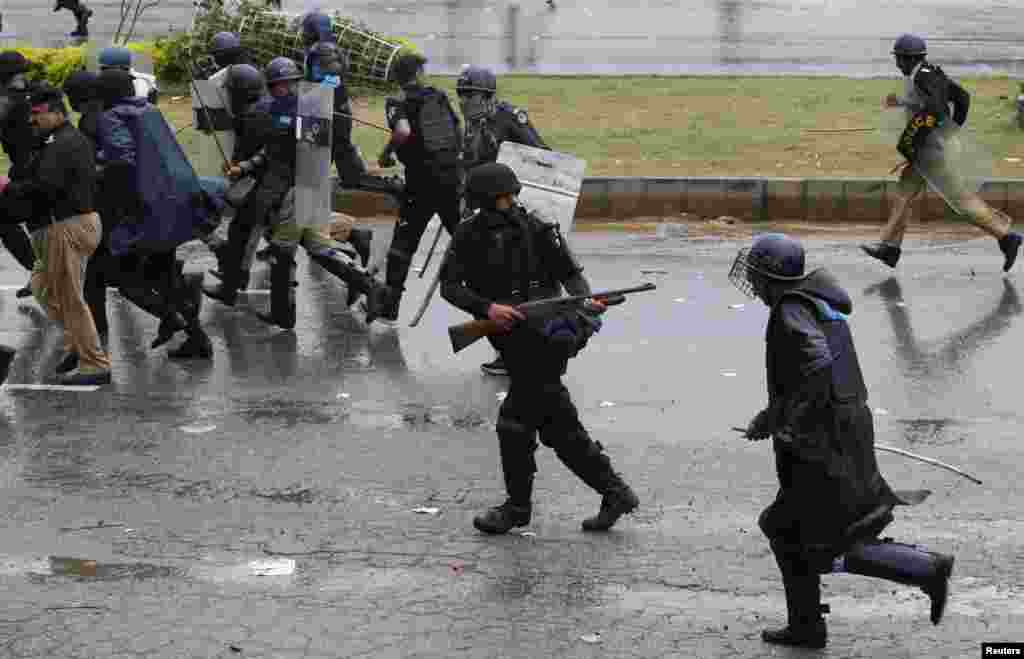 A police officer fires his weapon as he runs from demonstrators during the Revolution March towards the prime minister's house in Islamabad, Sept. 1, 2014.