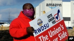 In this Tuesday, Feb. 9, 2021 file photo, Michael Foster of the Retail, Wholesale and Department Store Union holds a sign outside an Amazon facility where labor is trying to organize workers in Bessemer, Ala. 