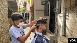 En un callejón del barrio caraqueño La Lucha, Jackner Quevedo atiende a un cliente en una improvisada barbería frente a su casa. Septiembre, 2021. Foto: Adriana Nuñez Rabascall - VOA.