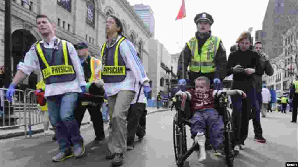 Polícia de Boston ajuda um menino ferido em Boylston Street enquanto paramédicos transportam um corredor ferido durante a explosão na Maratona de Boston 2013 (15 de Abril).