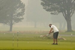A golfer wears a face mask as he practices his putting at the smoke-shrouded Lake Tahoe Golf Course in South Lake Tahoe, Calif., Aug. 24, 2021.