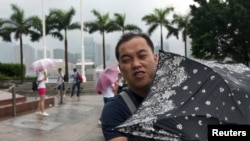 Seorang pria berusaha menahan terpaan angin dengan payungnya di Lapangan Golden Bauhinia, saat topan Utor mendekati Hong Kong (14/8).